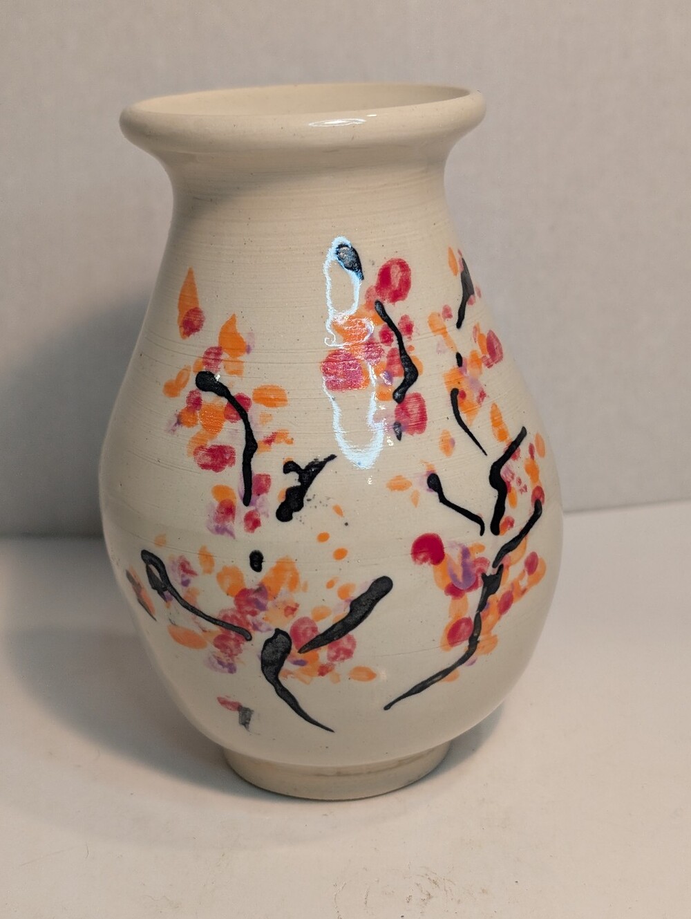 A white ceramic vase features a delicate, hand-painted cherry blossom design.